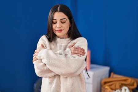 Photo for Young beautiful hispanic woman hugging himself touching softener sweater at laundry room - Royalty Free Image