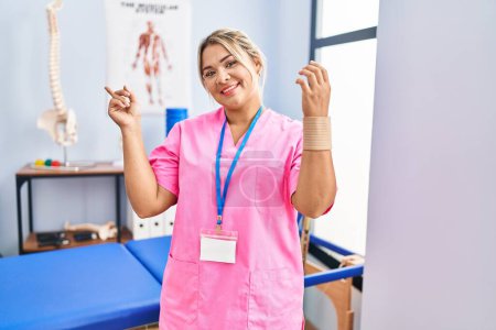 Photo for Young hispanic woman working at pain recovery clinic wearing wristband smiling happy pointing with hand and finger to the side - Royalty Free Image