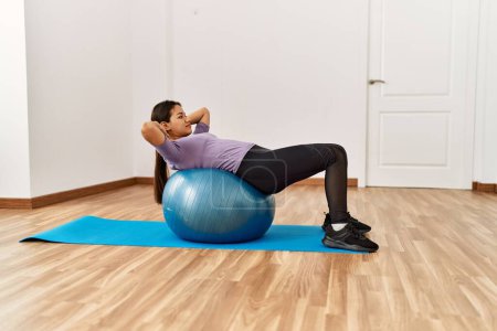Photo for Young latin woman doing abs exercise using fit ball at sport center - Royalty Free Image
