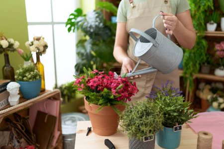 Téléchargez les photos : Jeune belle femme fleuriste arrosage plante à la boutique de fleurs - en image libre de droit