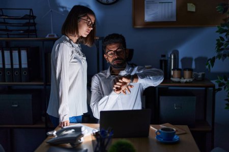 Man and woman business workers using laptop looking watch at office