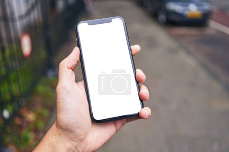 Téléchargez les photos : Homme tenant smartphone montrant écran blanc vierge à la rue - en image libre de droit