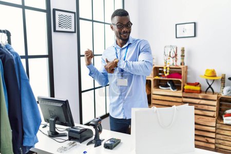 Foto de Joven hombre africano trabajando como gerente en una boutique minorista apuntando hacia atrás con la mano y los pulgares hacia arriba, sonriendo confiado - Imagen libre de derechos