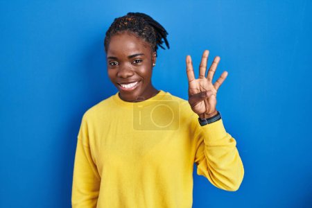 Foto de Beautiful black woman standing over blue background showing and pointing up with fingers number four while smiling confident and happy. - Imagen libre de derechos