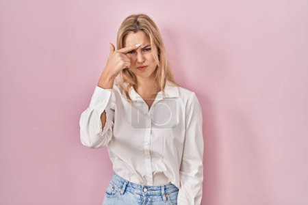 Photo for Young caucasian woman wearing casual white shirt over pink background pointing unhappy to pimple on forehead, ugly infection of blackhead. acne and skin problem - Royalty Free Image