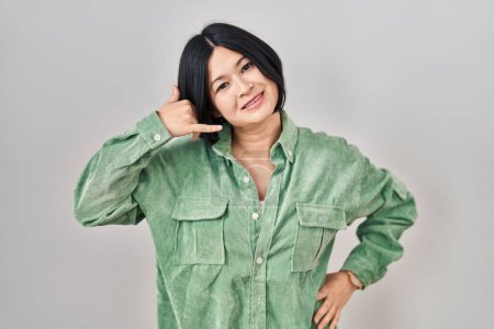Foto de Mujer asiática joven de pie sobre fondo blanco sonriendo haciendo gesto de teléfono con la mano y los dedos como hablar por teléfono. comunicar conceptos. - Imagen libre de derechos