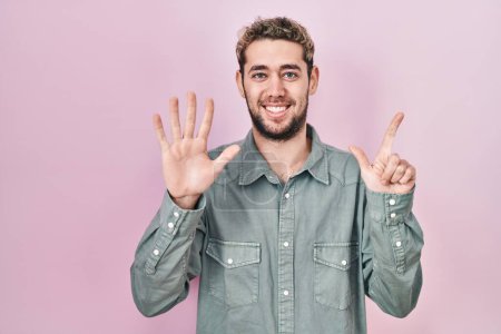 Téléchargez les photos : Homme hispanique avec barbe debout sur fond rose montrant et pointant vers le haut avec les doigts numéro sept tout en souriant confiant et heureux. - en image libre de droit