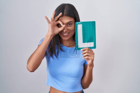 Photo for Brunette young woman holding l sign for new driver smiling happy doing ok sign with hand on eye looking through fingers - Royalty Free Image