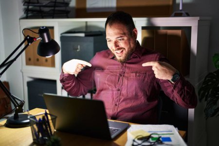 Foto de Hombre hispano de talla grande con barba trabajando en la oficina por la noche, con cara sonriente, señalándose con los dedos orgullosos y contentos. - Imagen libre de derechos