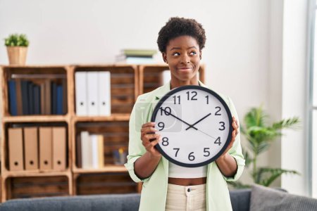 Photo for African american woman holding big clock smiling looking to the side and staring away thinking. - Royalty Free Image