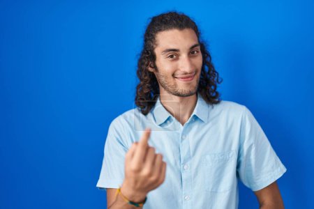 Téléchargez les photos : Young hispanic man standing over blue background beckoning come here gesture with hand inviting welcoming happy and smiling - en image libre de droit