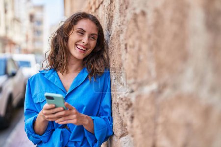 Foto de Mujer joven sonriendo confiada usando teléfono inteligente en la calle - Imagen libre de derechos