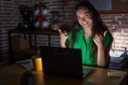 Photo for Young teenager girl working at the office at night success sign doing positive gesture with hand, thumbs up smiling and happy. cheerful expression and winner gesture. - Royalty Free Image