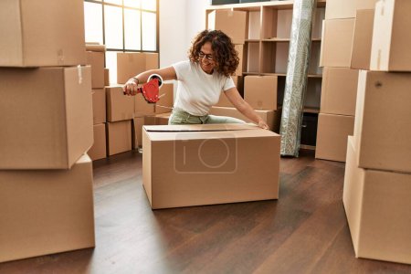 Photo for Middle age hispanic woman smiling confident packing cardboard box at new home - Royalty Free Image