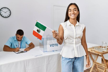 Téléchargez les photos : Jeune électrice mexicaine souriante heureuse tenant le drapeau mexicain au collège électoral. - en image libre de droit