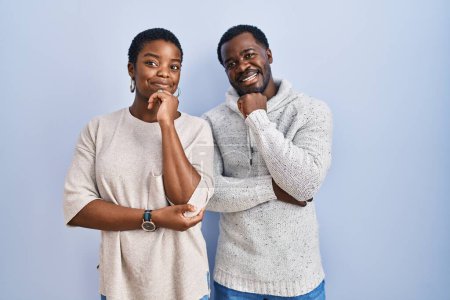 Photo for Young african american couple standing over blue background together with hand on chin thinking about question, pensive expression. smiling and thoughtful face. doubt concept. - Royalty Free Image