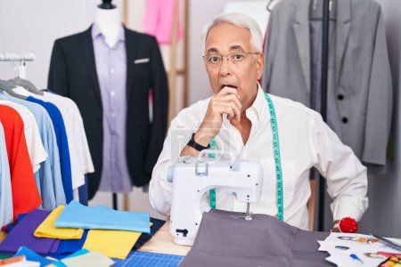 Photo for Middle age man with grey hair dressmaker using sewing machine looking fascinated with disbelief, surprise and amazed expression with hands on chin - Royalty Free Image