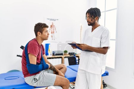 Photo for Two men physiptherapist and patient having rehab session writing accident report at clinic - Royalty Free Image