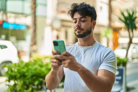 Téléchargez les photos : Jeune homme hispanique utilisant un smartphone dans la rue - en image libre de droit