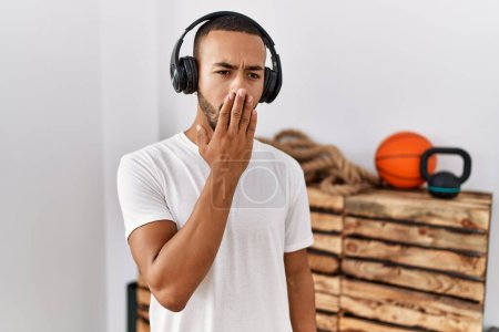 Téléchargez les photos : Afro-Américain écoutant de la musique à l'aide d'écouteurs à la salle de gym ennuyé bâillement fatigué couvrant la bouche avec la main. agitation et somnolence. - en image libre de droit