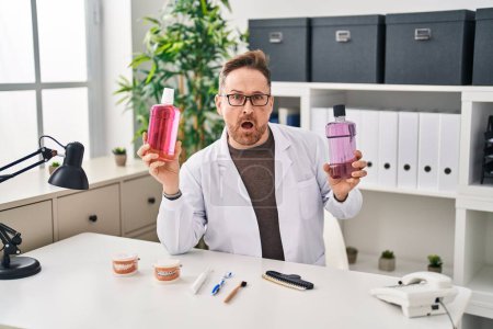 Photo for Middle age caucasian dentist man holding mouthwash for fresh breath in shock face, looking skeptical and sarcastic, surprised with open mouth - Royalty Free Image