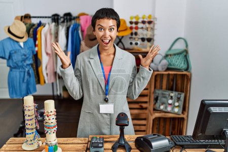 Photo for Young hispanic woman with short hair working as manager at retail boutique celebrating crazy and amazed for success with arms raised and open eyes screaming excited. winner concept - Royalty Free Image