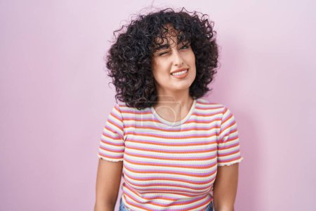 Téléchargez les photos : Jeune femme du Moyen-Orient debout sur fond rose clin d'oeil en regardant la caméra avec une expression sexy, gai et heureux visage. - en image libre de droit