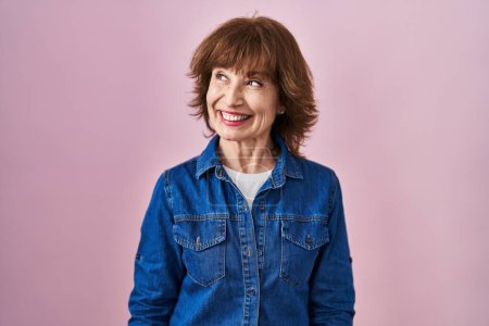 Photo for Middle age woman standing over pink background smiling looking to the side and staring away thinking. - Royalty Free Image