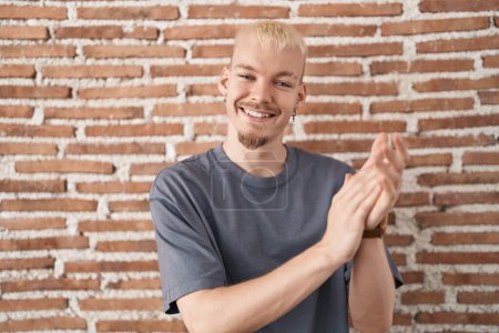 Téléchargez les photos : Jeune homme caucasien debout sur le mur de briques applaudissant heureux et joyeux, souriant mains fières ensemble - en image libre de droit