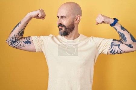 Photo for Hispanic man with tattoos standing over yellow background showing arms muscles smiling proud. fitness concept. - Royalty Free Image