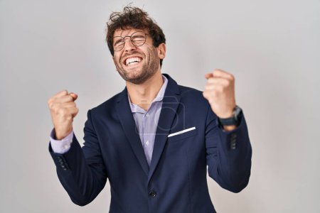 Foto de Hombre de negocios hispano con gafas muy contentos y emocionados haciendo gesto ganador con los brazos levantados, sonriendo y gritando por el éxito. concepto de celebración. - Imagen libre de derechos