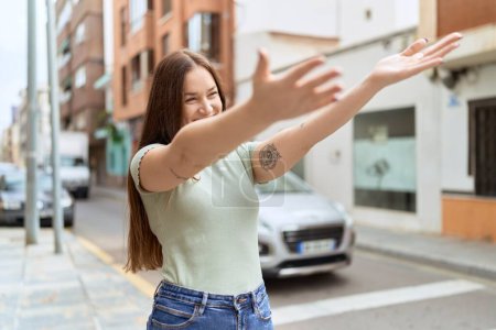 Téléchargez les photos : Jeune belle femme souriante confiante faisant geste câlin avec les bras à la rue - en image libre de droit