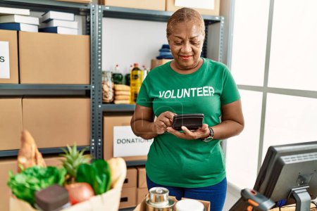 Foto de Mujer afroamericana mayor con uniforme de voluntaria usando calculadora en el centro de caridad - Imagen libre de derechos