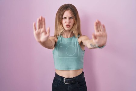 Photo for Blonde caucasian woman standing over pink background doing stop gesture with hands palms, angry and frustration expression - Royalty Free Image