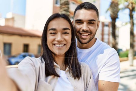 Photo pour Jeune couple latin souriant heureux et câlin faire selfie par la caméra à la ville. - image libre de droit