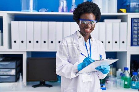 Photo for Young african american woman scientist writing on document at laboratory - Royalty Free Image