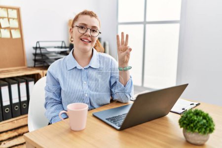 Photo for Young redhead woman working at the office using computer laptop showing and pointing up with fingers number three while smiling confident and happy. - Royalty Free Image