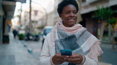 Téléchargez les photos : Jeune femme afro-américaine souriante confiante en utilisant un smartphone dans la rue - en image libre de droit