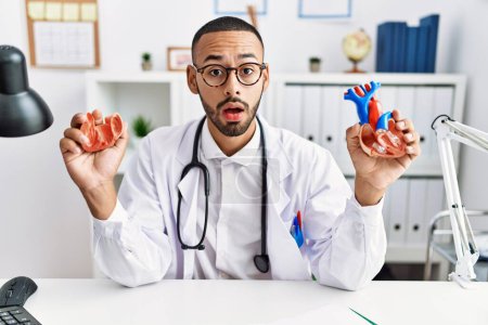 Photo for African american doctor man holding anatomical heart at the clinic clueless and confused expression. doubt concept. - Royalty Free Image