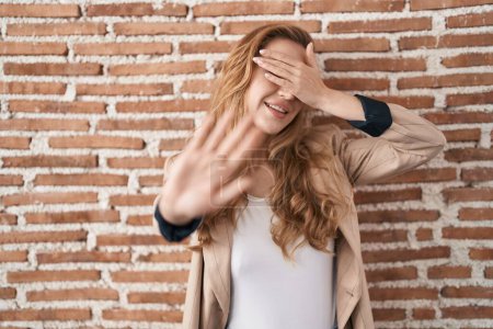 Foto de Beautiful blonde woman standing over bricks wall covering eyes with hands and doing stop gesture with sad and fear expression. embarrassed and negative concept. - Imagen libre de derechos