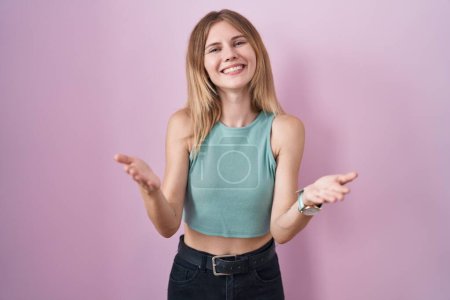 Photo for Blonde caucasian woman standing over pink background smiling cheerful offering hands giving assistance and acceptance. - Royalty Free Image