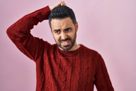 Photo for Young hispanic man with beard wearing casual sweater over pink background confuse and wonder about question. uncertain with doubt, thinking with hand on head. pensive concept. - Royalty Free Image