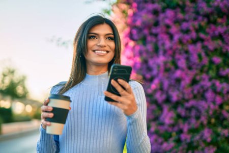 Téléchargez les photos : Jeune femme hispanique utilisant un smartphone et buvant une tasse de café près du parc - en image libre de droit