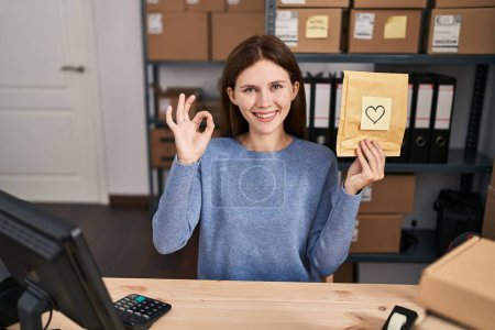 Photo for Young brunette woman working at small business ecommerce doing ok sign with fingers, smiling friendly gesturing excellent symbol - Royalty Free Image