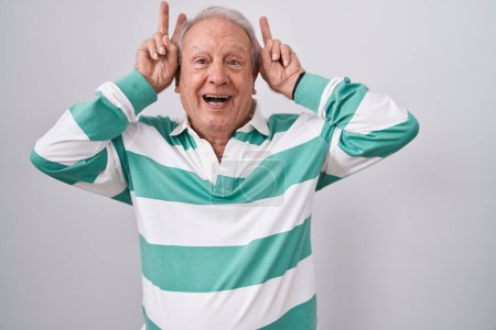Photo for Senior man with grey hair standing over white background posing funny and crazy with fingers on head as bunny ears, smiling cheerful - Royalty Free Image