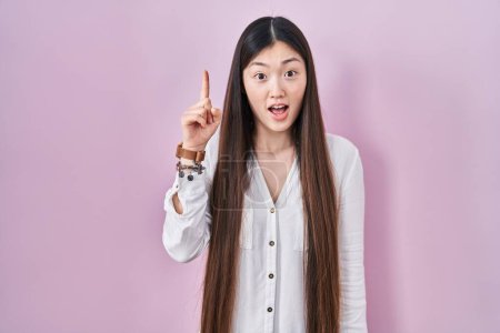 Téléchargez les photos : Jeune femme chinoise debout sur fond rose pointant du doigt avec une idée réussie. Sorti et heureux. numéro un. - en image libre de droit