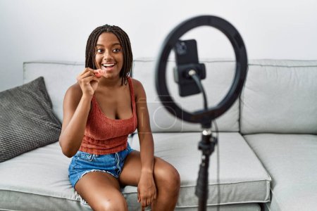 Téléchargez les photos : Jeune femme afro-américaine tenant la coupe menstruelle enregistrement tutoriel vidéo à la maison - en image libre de droit