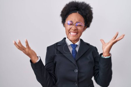 Téléchargez les photos : Belle femme africaine avec les cheveux bouclés portant une veste d'affaires et des lunettes célébrant fou et étonné pour le succès avec les bras levés et les yeux ouverts hurlant excités. concept gagnant - en image libre de droit