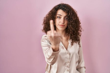 Photo for Hispanic woman with curly hair standing over pink background showing middle finger, impolite and rude fuck off expression - Royalty Free Image