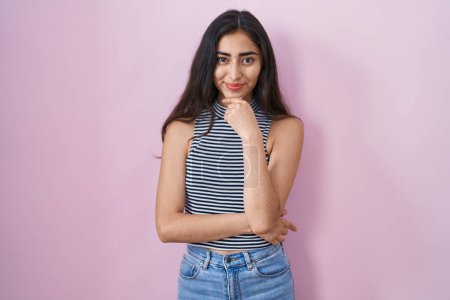 Foto de Young teenager girl wearing casual striped t shirt looking confident at the camera with smile with crossed arms and hand raised on chin. thinking positive. - Imagen libre de derechos
